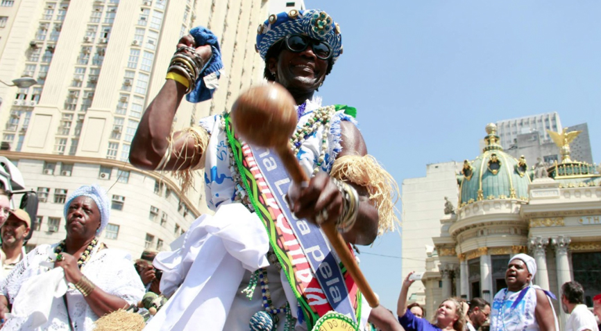 Passista vestido a caráter da umbanda dançando no centro da cidade, em frente ao municipal com o resto do bloco 